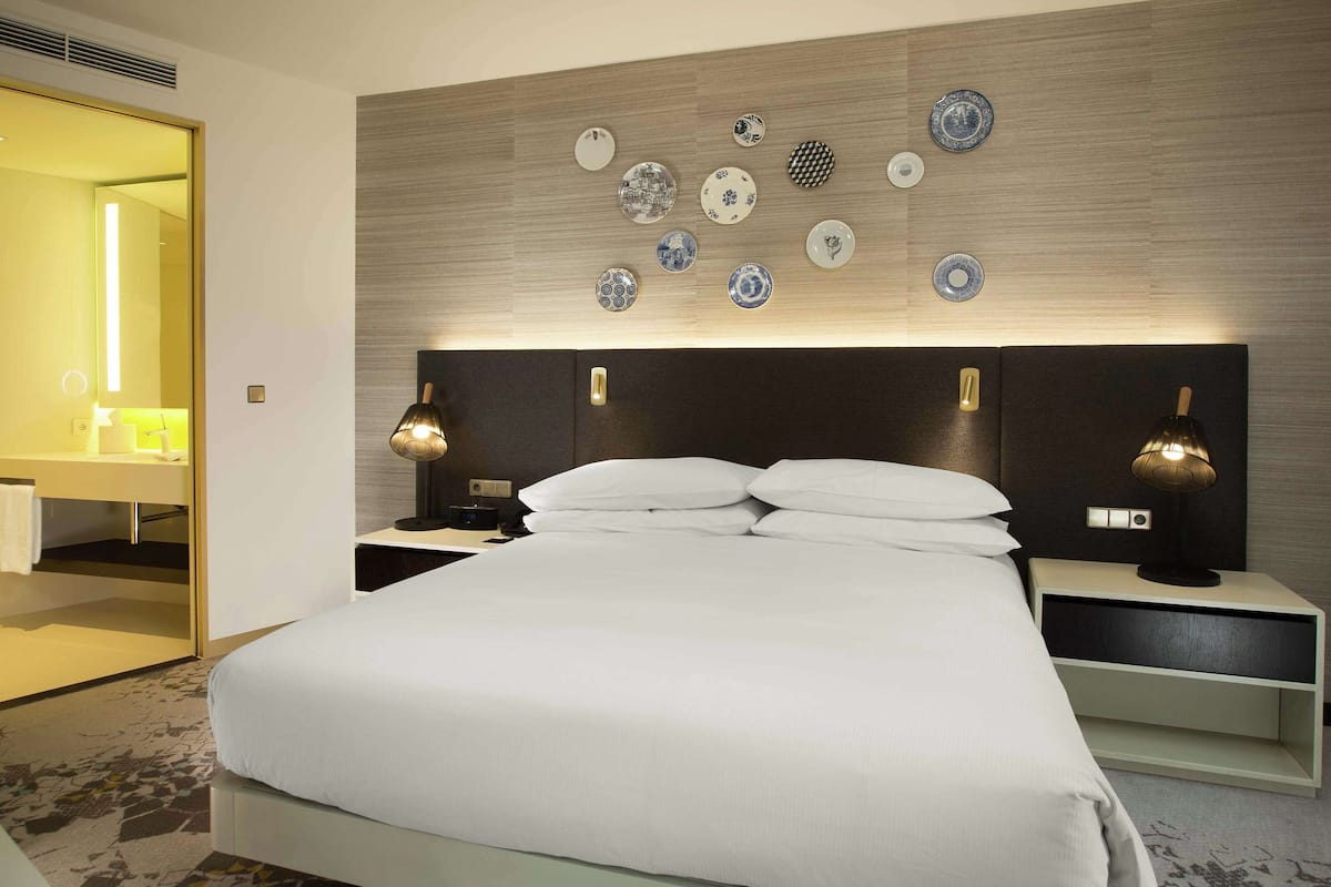 Habitación de hotel con una cama grande, dos mesitas de noche con lámparas, una luz en la pared y un espejo.