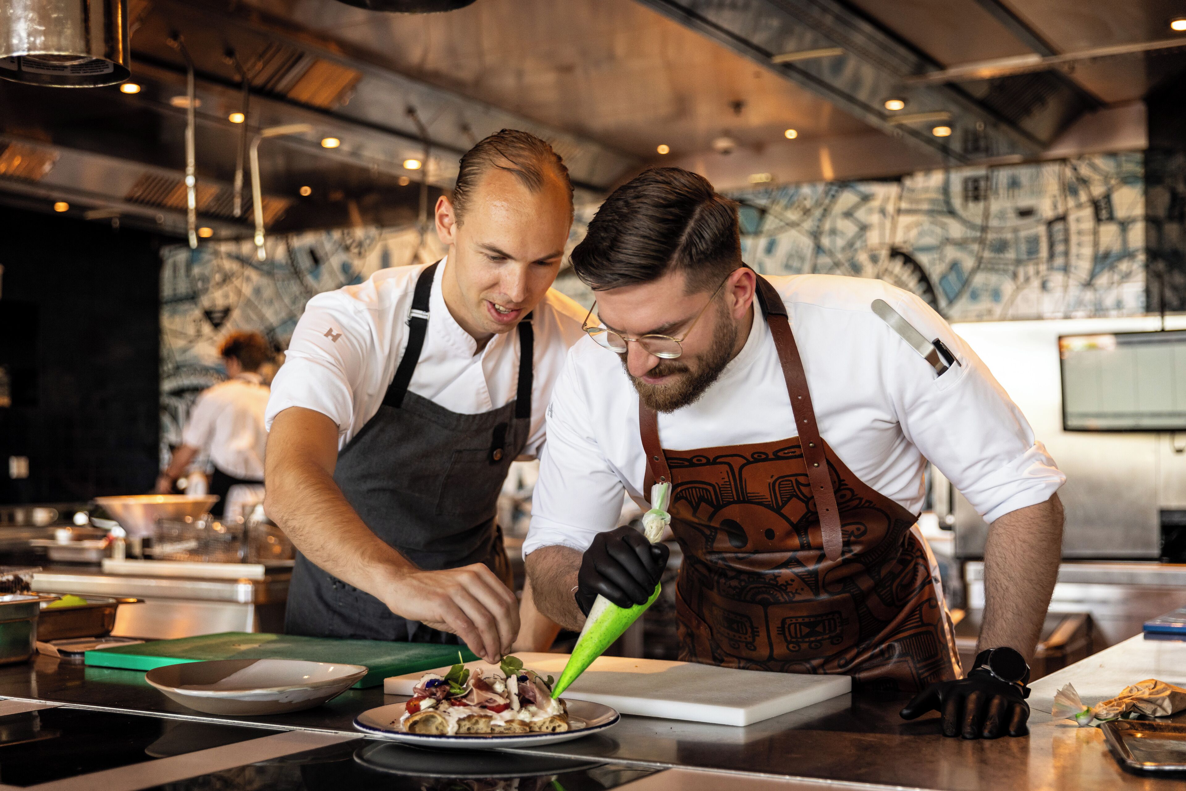 Two chefs preparing food in a modern kitchen with industrial design elements.