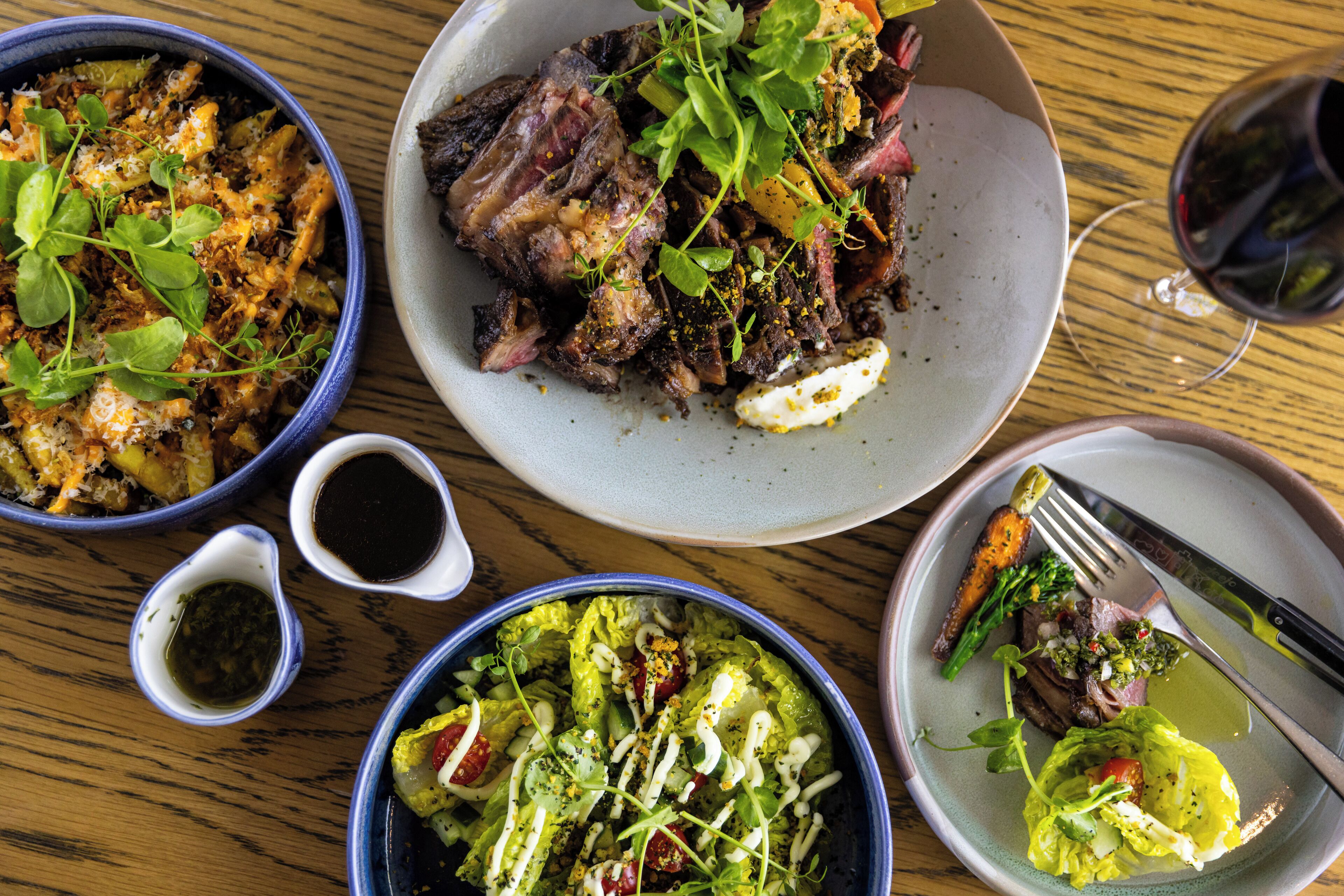 Una mesa con varios platos, incluyendo un tazón de ensalada, un plato de carne y un bol de pasta.