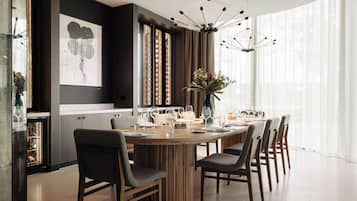 A modern dining area with a round wooden table, dark chairs, and a contemporary chandelier.