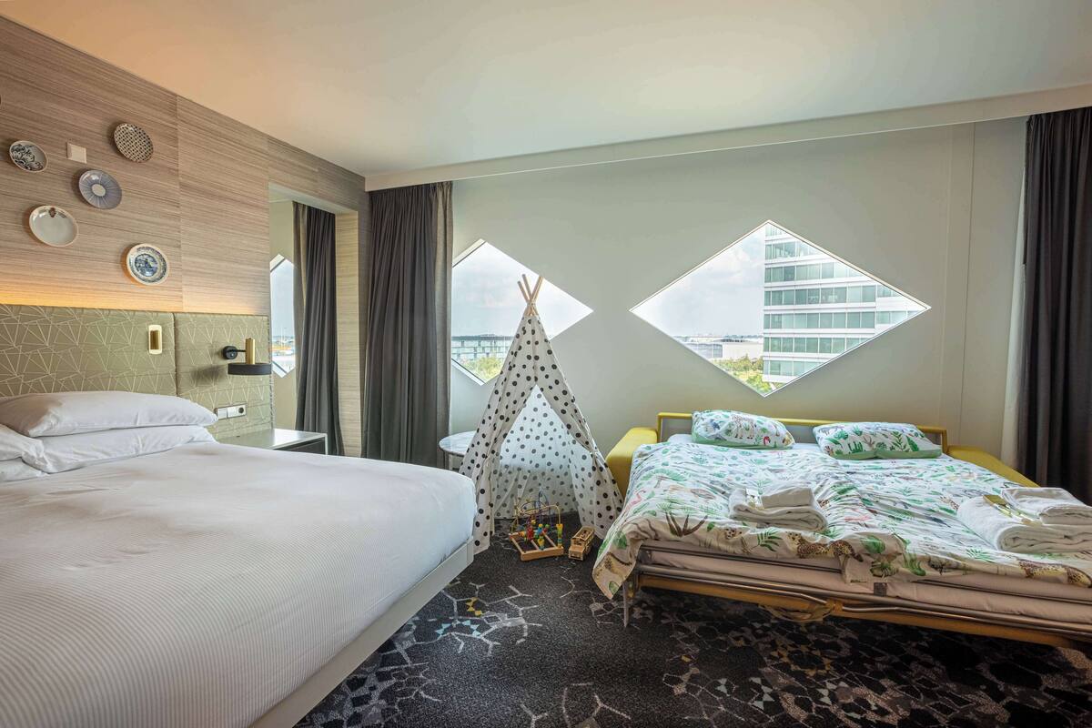Habitación de hotel con dos camas, una tienda tipi y vistas a un edificio a través de una ventana.