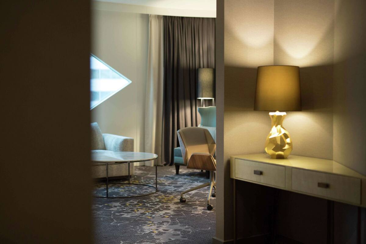 Habitación de hotel con escritorio, silla, lámpara y vistas al exterior a través de una ventana.