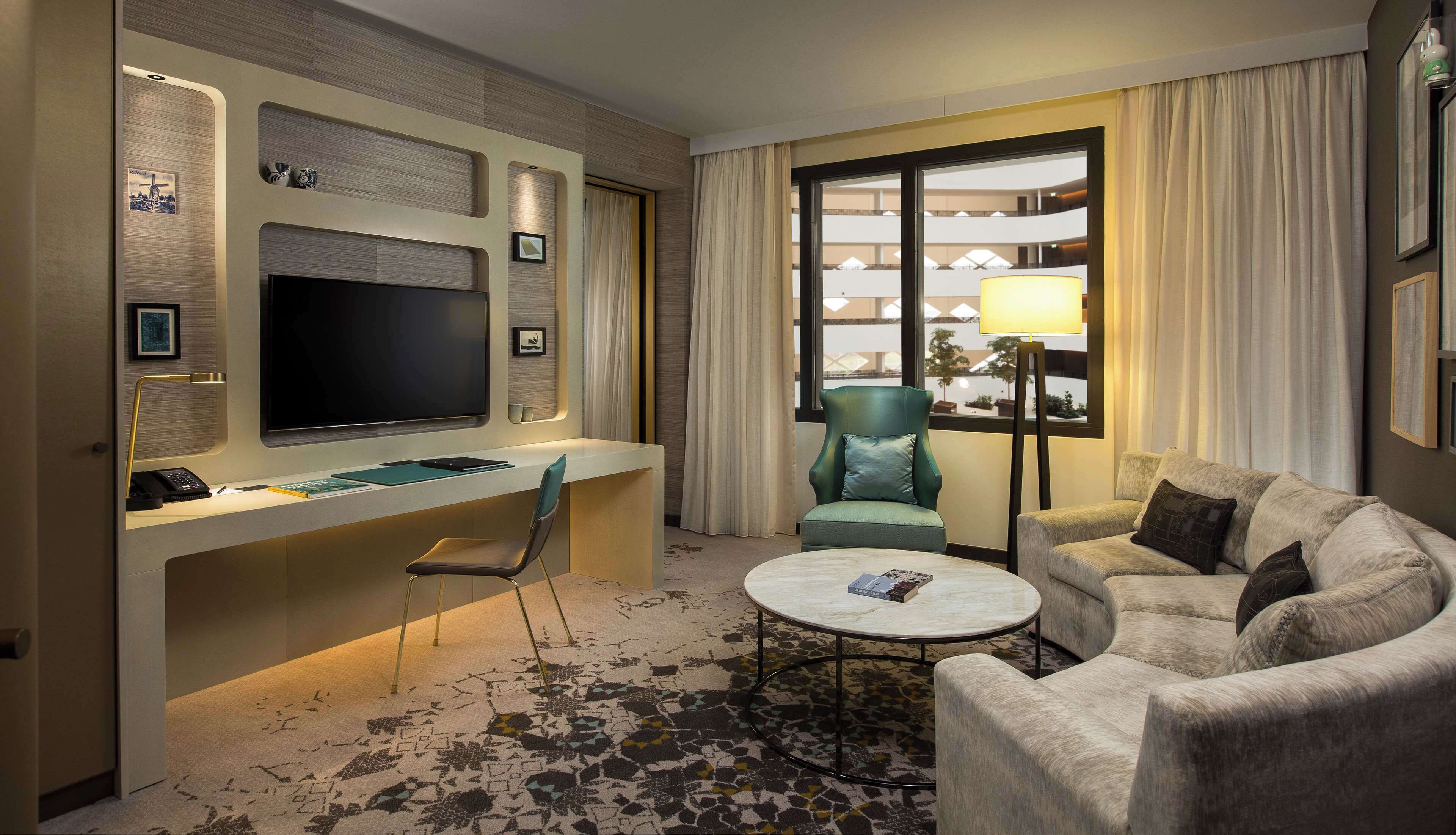 A hotel room with a desk, a flat-screen TV, a comfortable sofa, a chair, and a coffee table.