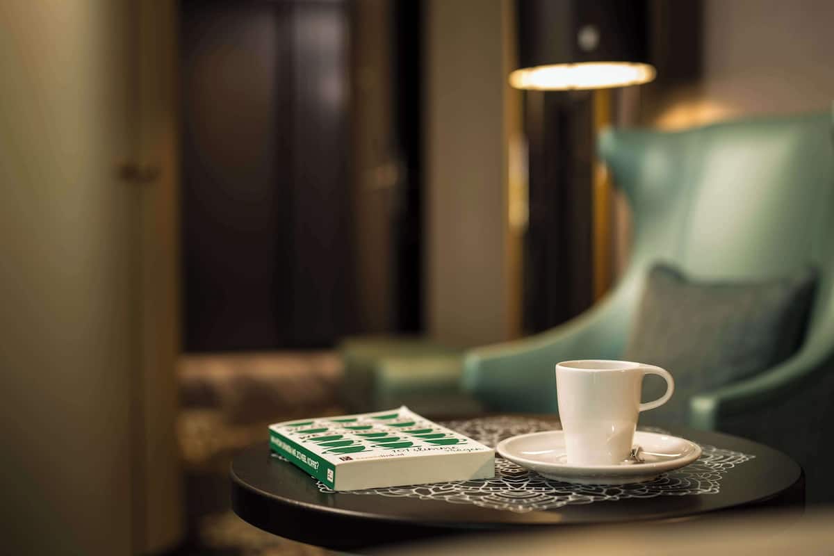Una mesa con una taza y platillo blancos, una caja verde y una bandeja estampada.