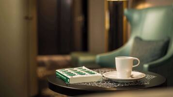 Uma mesa com uma xícara e pires brancos, uma caixa verde e um tabuleiro estampado.