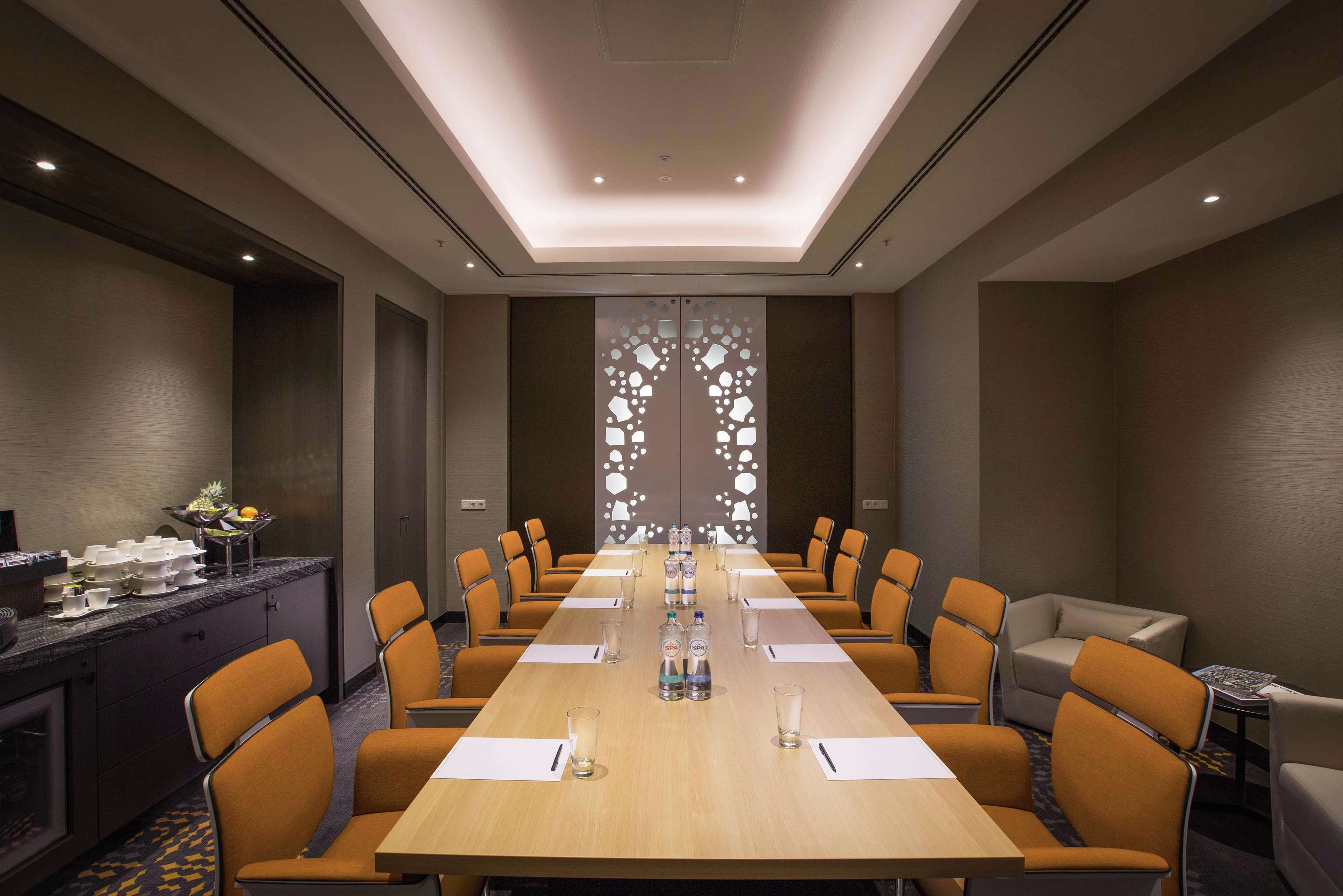 A conference room with a long table, orange chairs, water bottles, and a decorative wall panel.