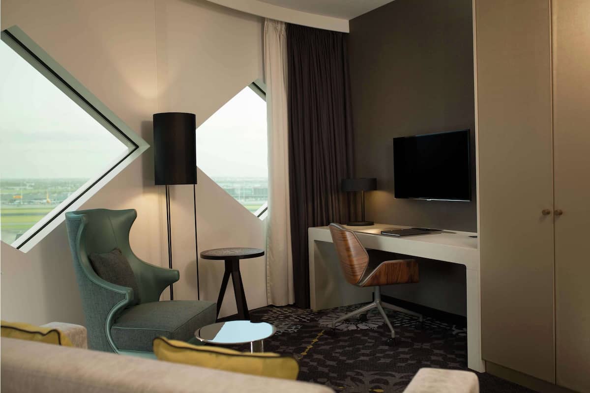 Habitación de hotel con un ventanal grande, un escritorio, una silla, un televisor y una mesita.