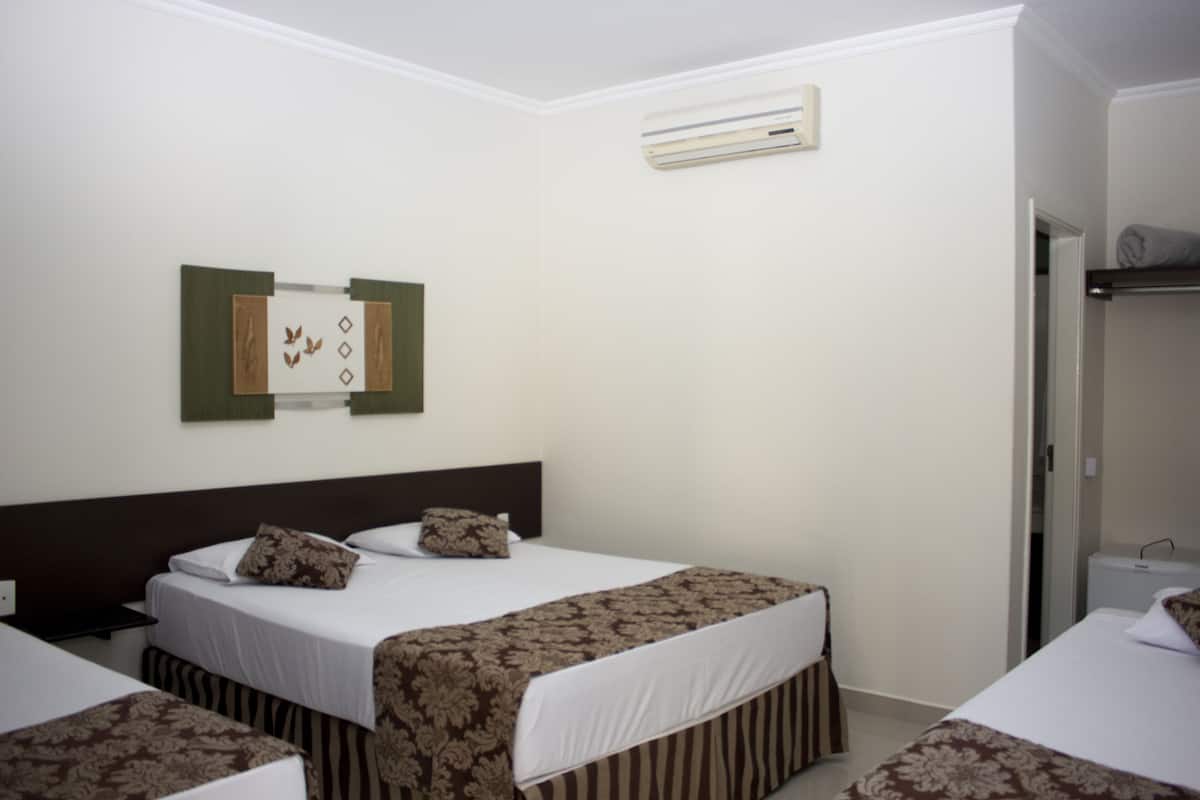 A hotel room with two beds, a wall-mounted air conditioner, and a framed picture.