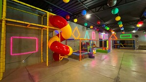 An indoor play area with colorful slides and play structures, neon-lit walls, and a concrete floor. - Hotel Dolce Dulce (Olímpia)
