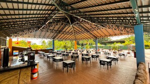 An outdoor dining area with tables and chairs, a bar, and a view of a pool and greenery. - Hotel Dolce Dulce (Olímpia)