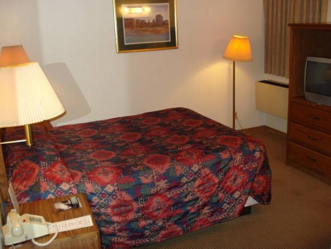 Habitación de hotel con cama, escritorio con lámpara, televisión e imagen en la pared.