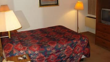 Habitación de hotel con cama, escritorio con lámpara, televisión e imagen en la pared.