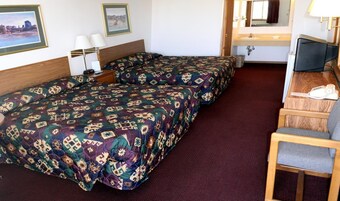 Habitación de hotel con dos camas, un escritorio con silla, televisor y baño con lavamanos y espejo.