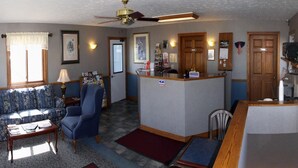 A living room with a sofa, armchair, coffee table, and a small dining area. There is a kitchen area with a refrigerator and microwave. - Yorkshire Motel (York)