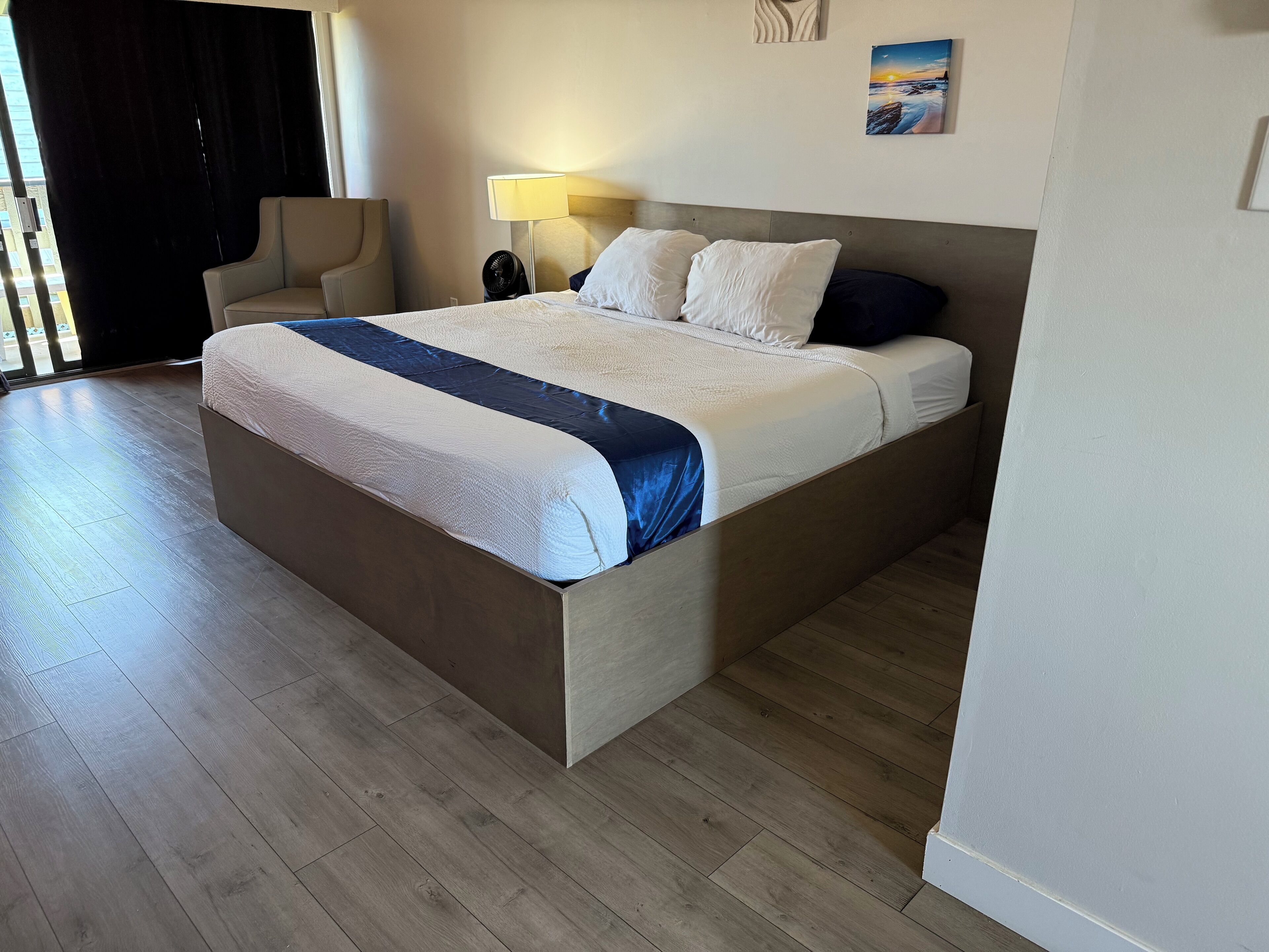 A modern hotel room with a large bed, a chair, a nightstand, and a lamp.