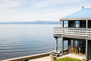 A lakeside building with a balcony, seating area, and a view of the water.