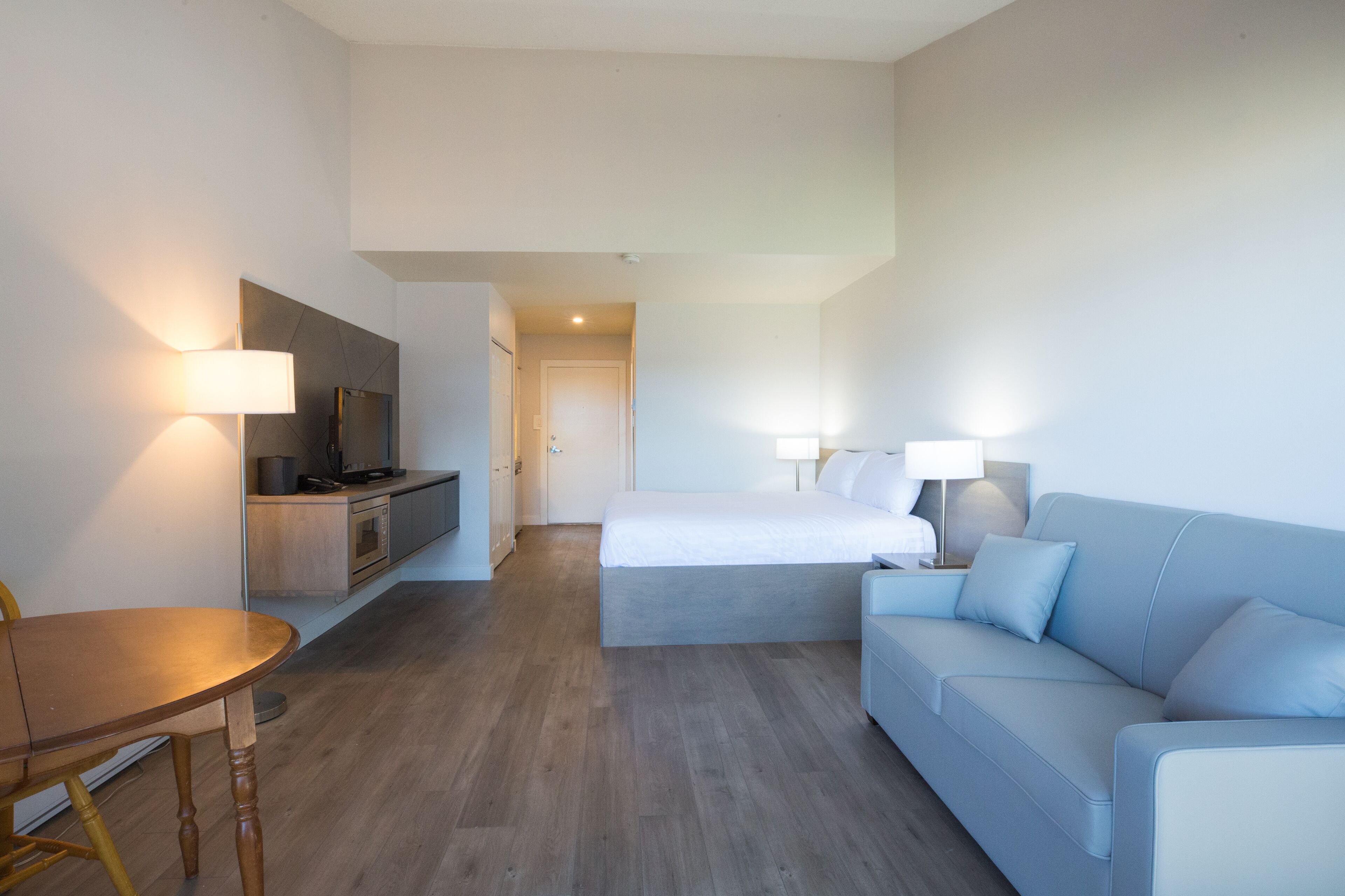 Quarto de hotel com cama, sofá, mesa de jantar e cozinha compacta.