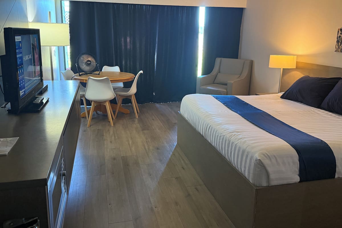 A hotel room with a bed, a desk with a computer, a chair, and a dining table.