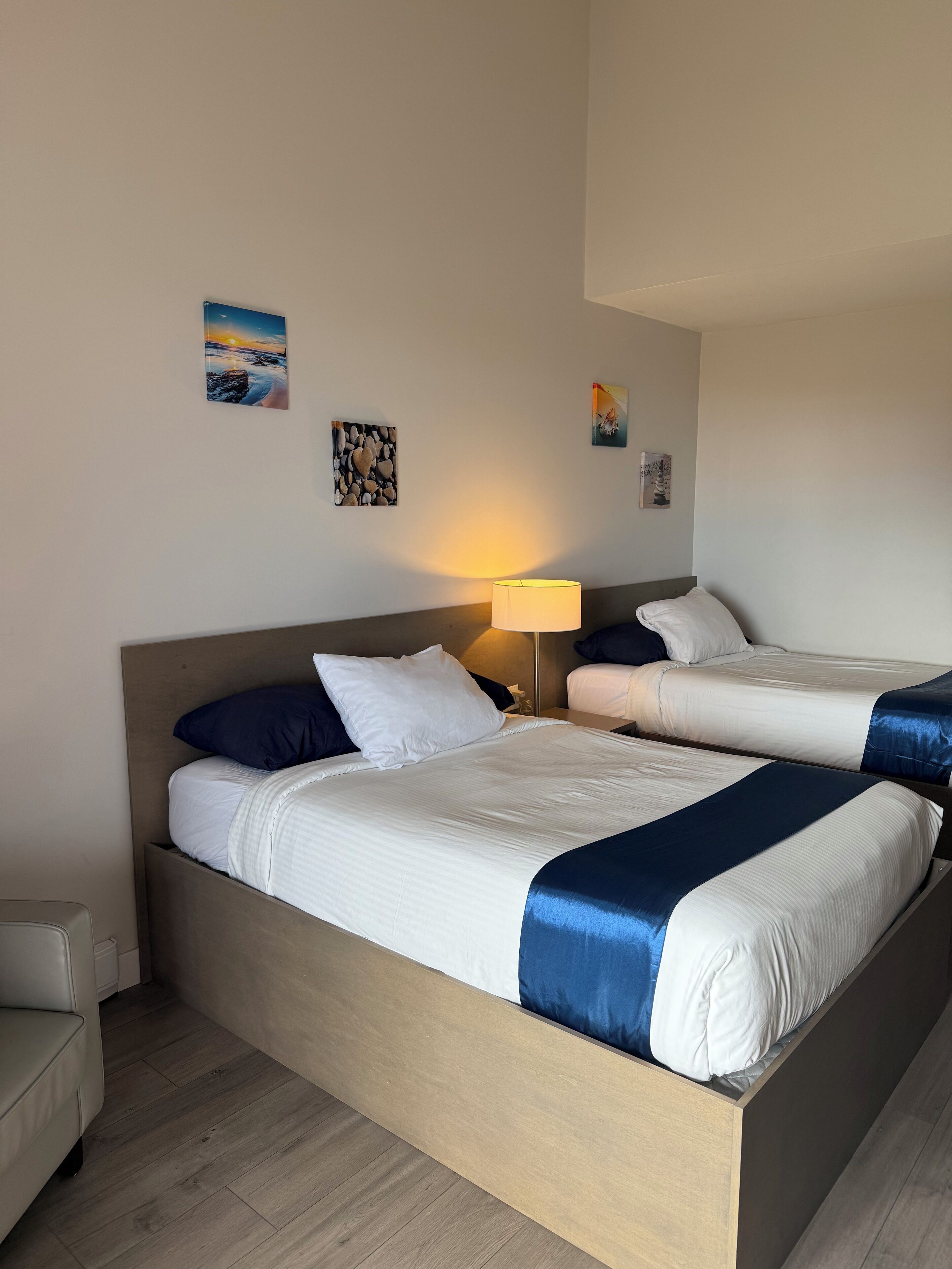 A hotel room with two beds, a nightstand, a lamp, and wall art.