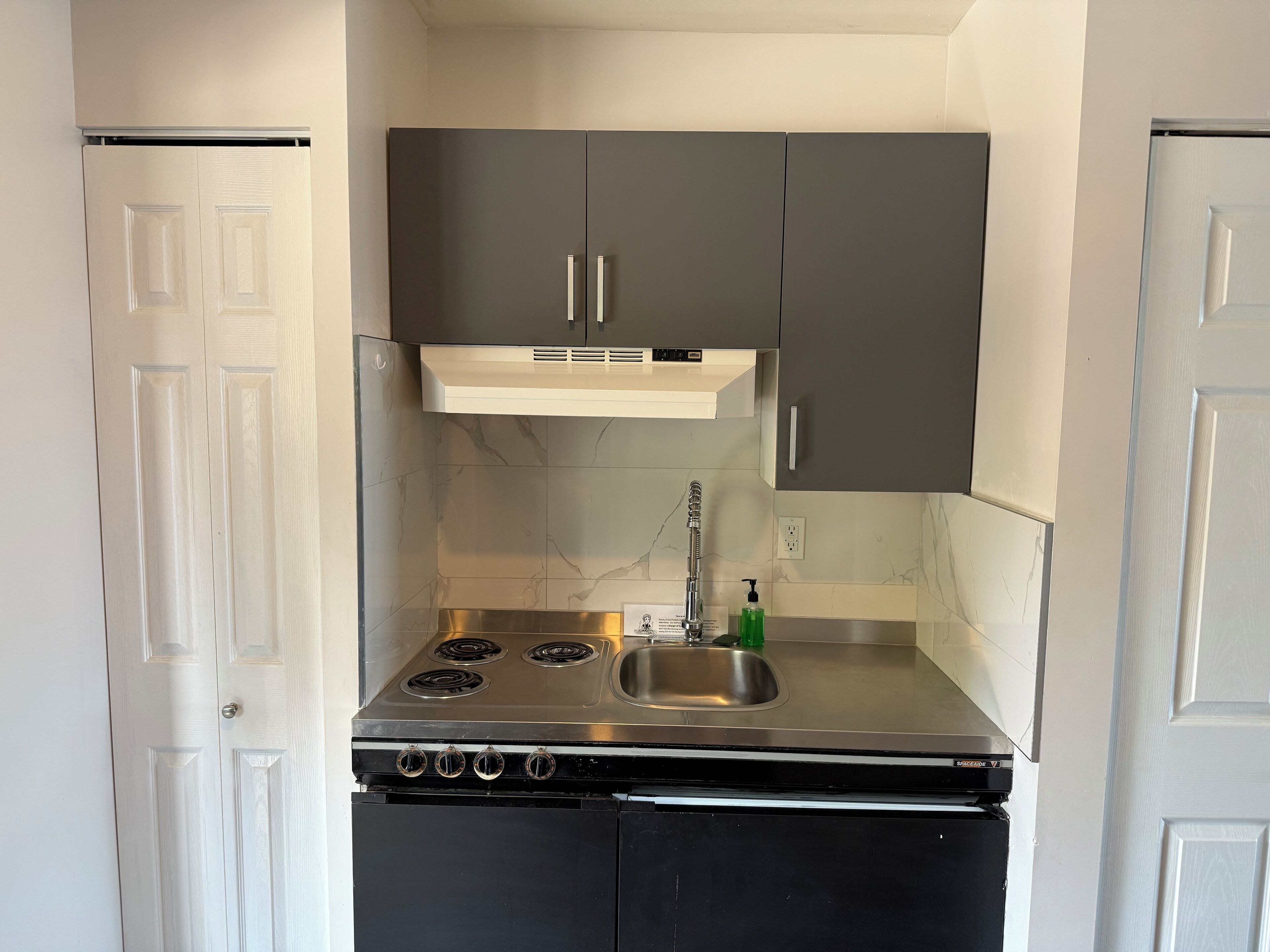 Une cuisine de taille réduite, équipée d’une cuisinière, d’un évier et de meubles de rangement de couleur sombre.