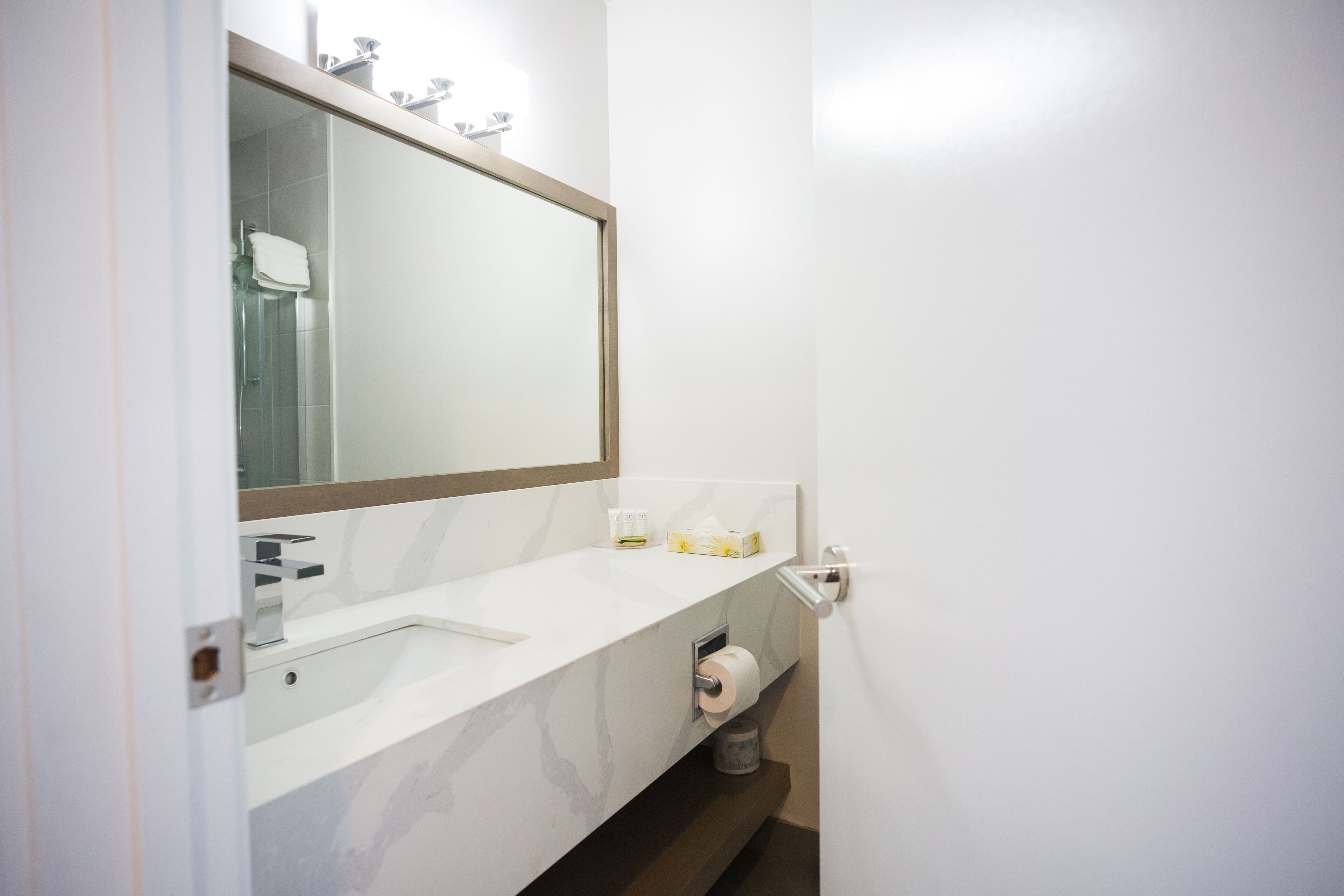Ein Badezimmer mit einem weißen Waschbecken, einem großen Spiegel und einem Toilettenpapierhalter.