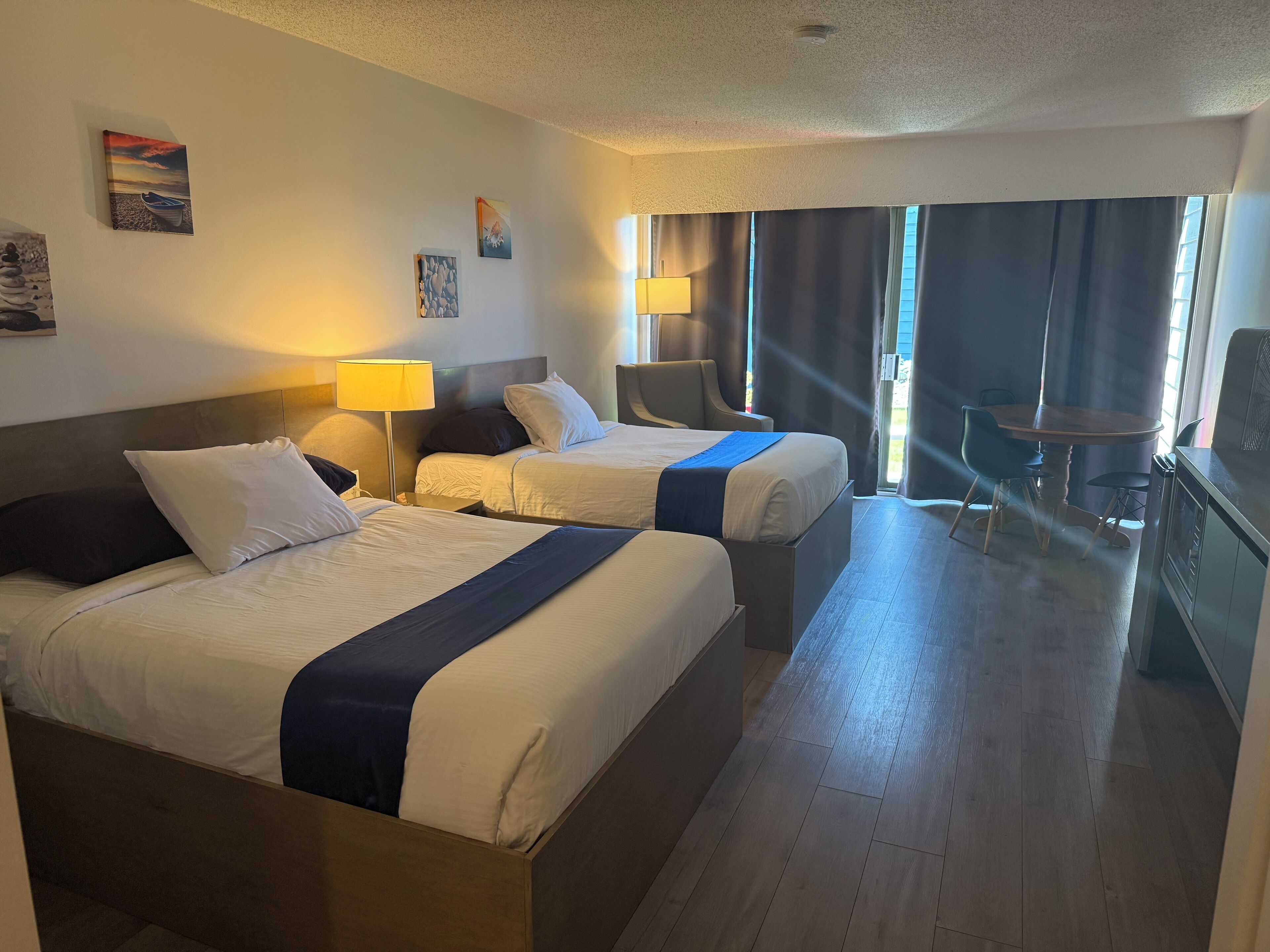A hotel room with two beds, a desk, and a dining area.