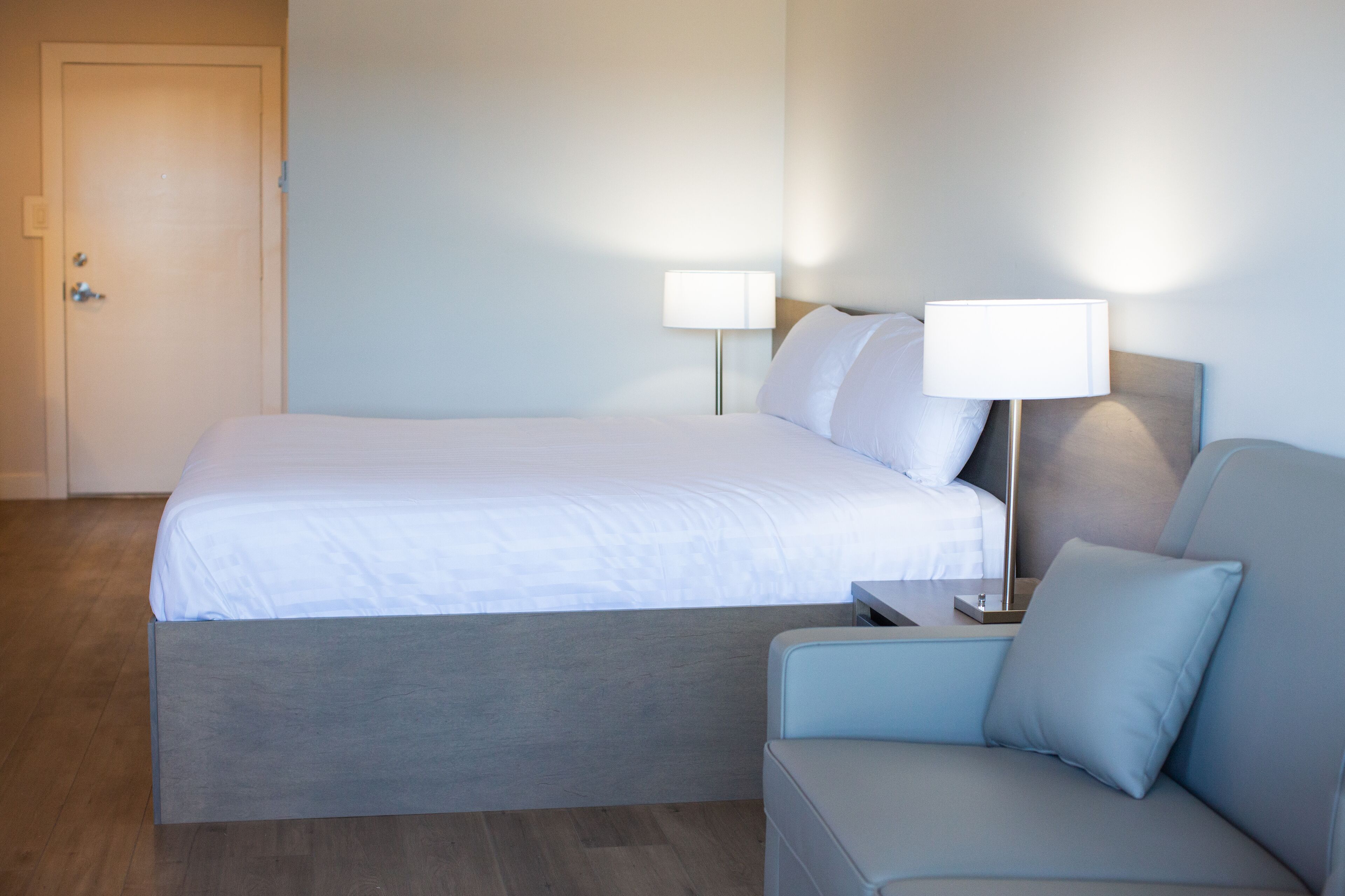 Una habitación de hotel con una cama, una mesita de noche, una lámpara y un sofá.