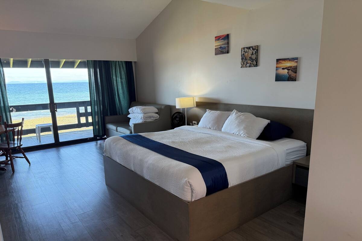 A hotel room with a large bed, a desk, a chair, and a view of the beach.