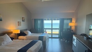 Une chambre d’hôtel avec deux lits, un bureau, une chaise, une télévision et une vue sur la plage.