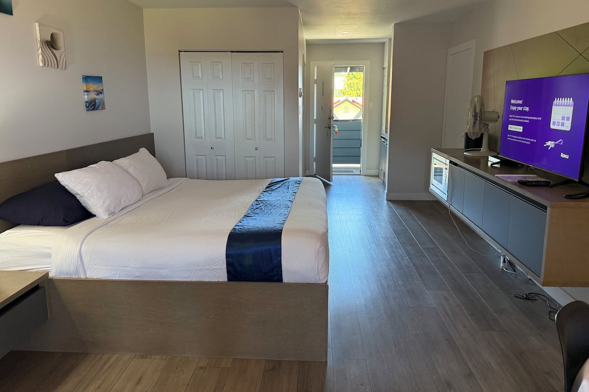 A hotel room with a bed, a desk, a TV, and a view of the outside.
