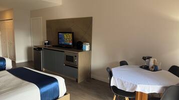 A hotel room with a bed, a small kitchenette, a dining table with chairs, and a television.