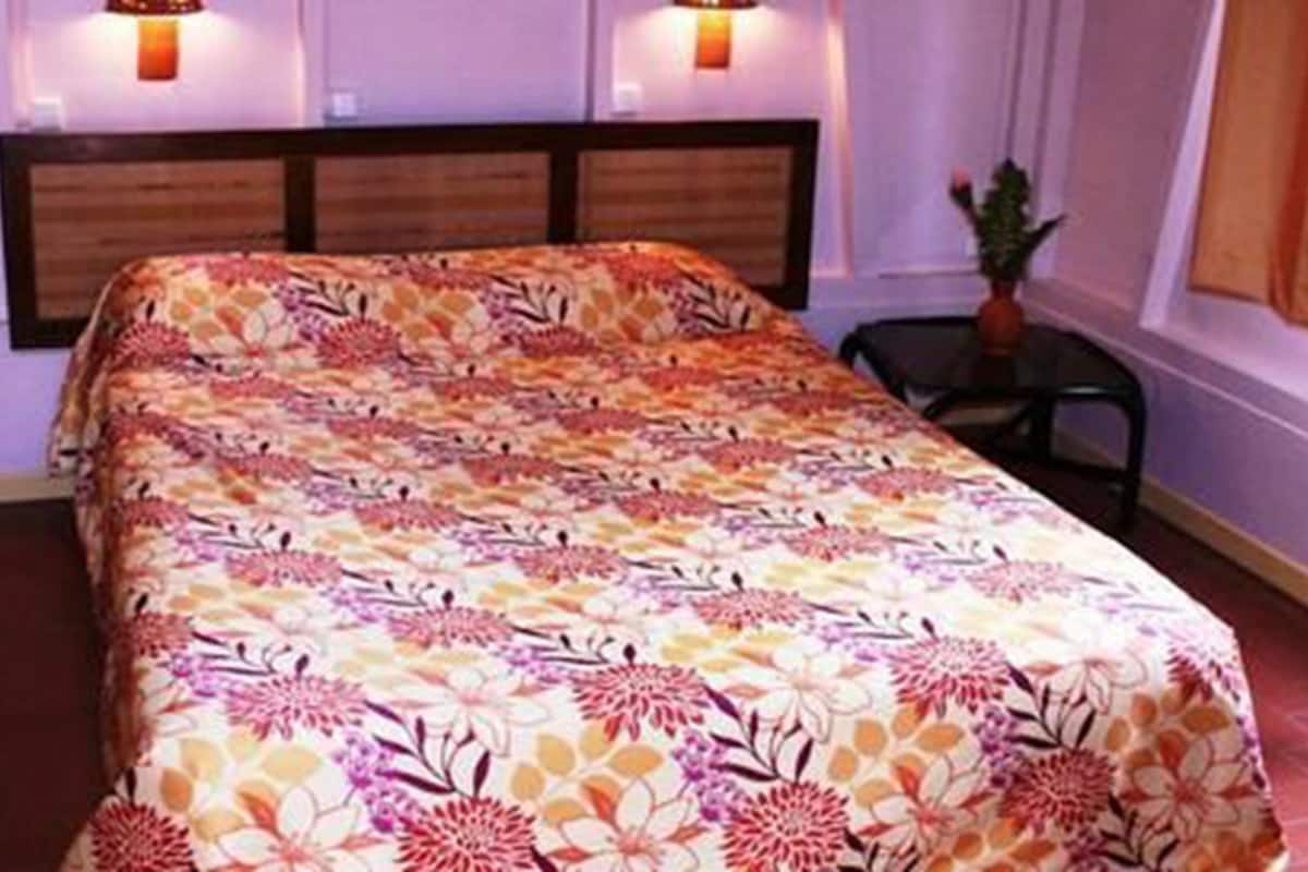 A bed with a floral bedspread, a wooden headboard, and two wall-mounted lamps.