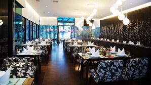 Um restaurante com um balcão comprido, várias mesas e cadeiras com estofamento floral.