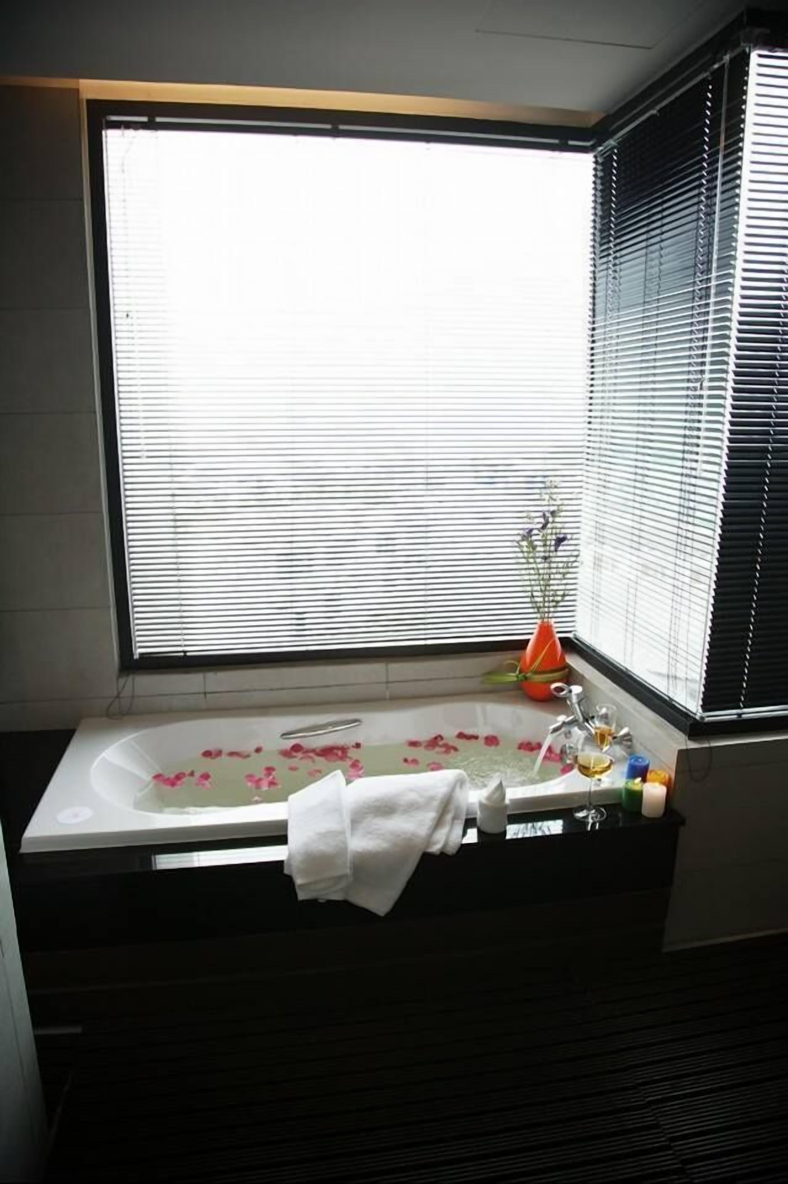 A bathroom with a bathtub, a window with blinds, and a vase with flowers.