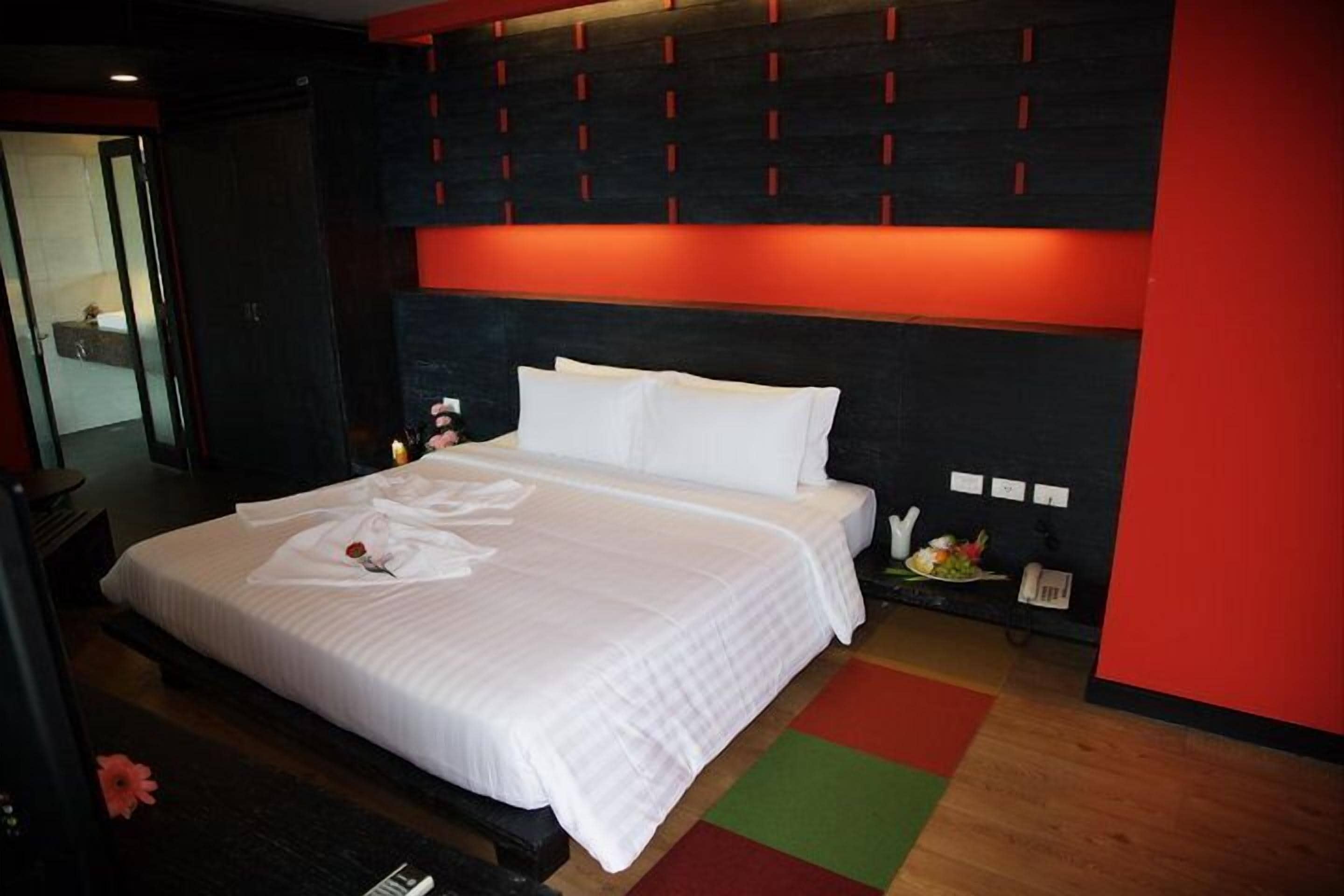 A neatly made bed with white linens and pillows, a bedside table with a lamp, and a wall-mounted phone.