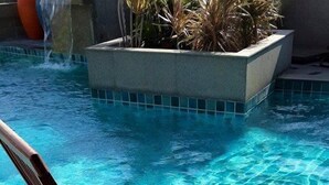 Uma cadeira de estar de madeira junto a uma piscina, com um copo de bebida e uma garrafa.
