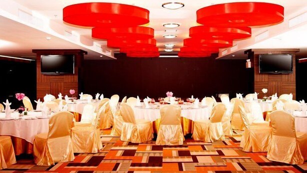 A banquet hall with round tables, white tablecloths, and chairs with golden sashes. - The Sez Hotel (Chonburi)