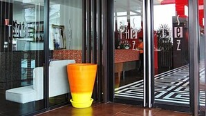 Um hall de hotel moderno com divisória de vidro, um vaso amarelo e piso estampado.