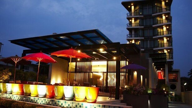 Um hotel moderno com terraço no telhado, área externa com assentos e guarda-sóis, e um edifício com várias andares e varandas.