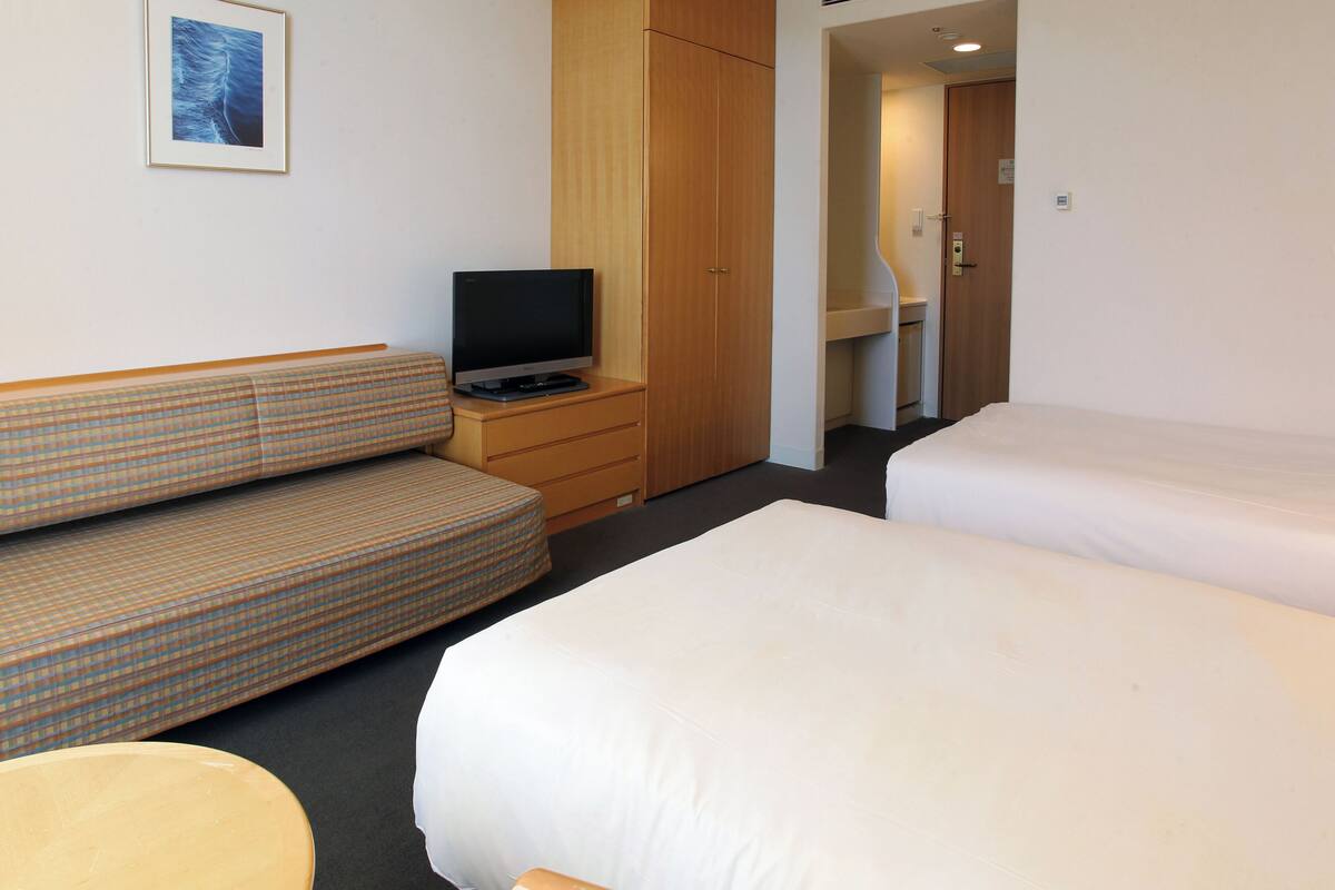 A hotel room with a sofa, a TV on a wooden cabinet, a bed, and a bathroom visible through an open door.