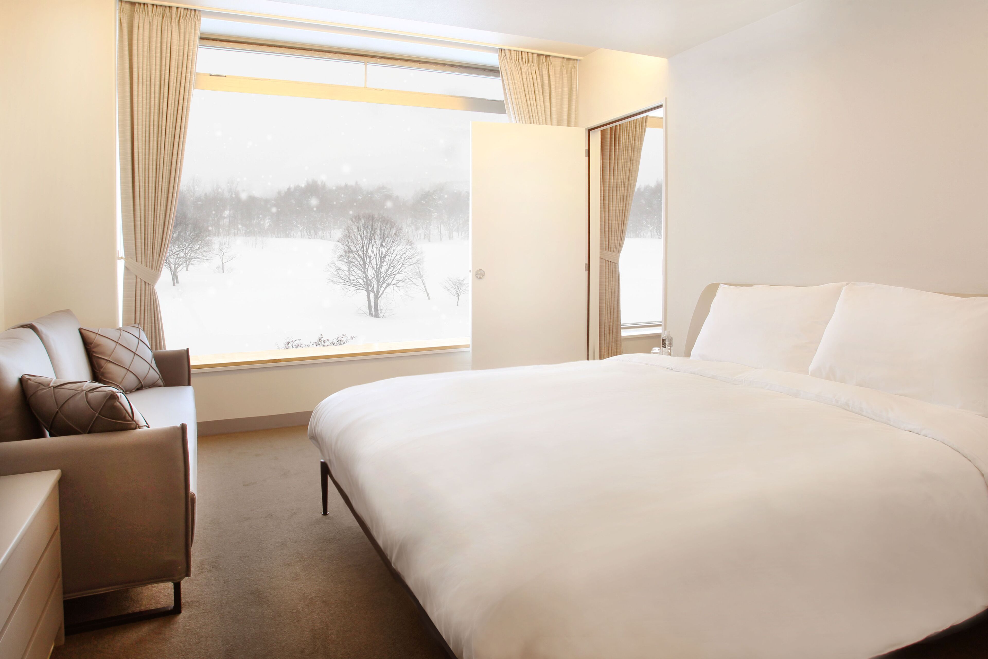 A hotel room with a large bed, a sofa, and a window with curtains.