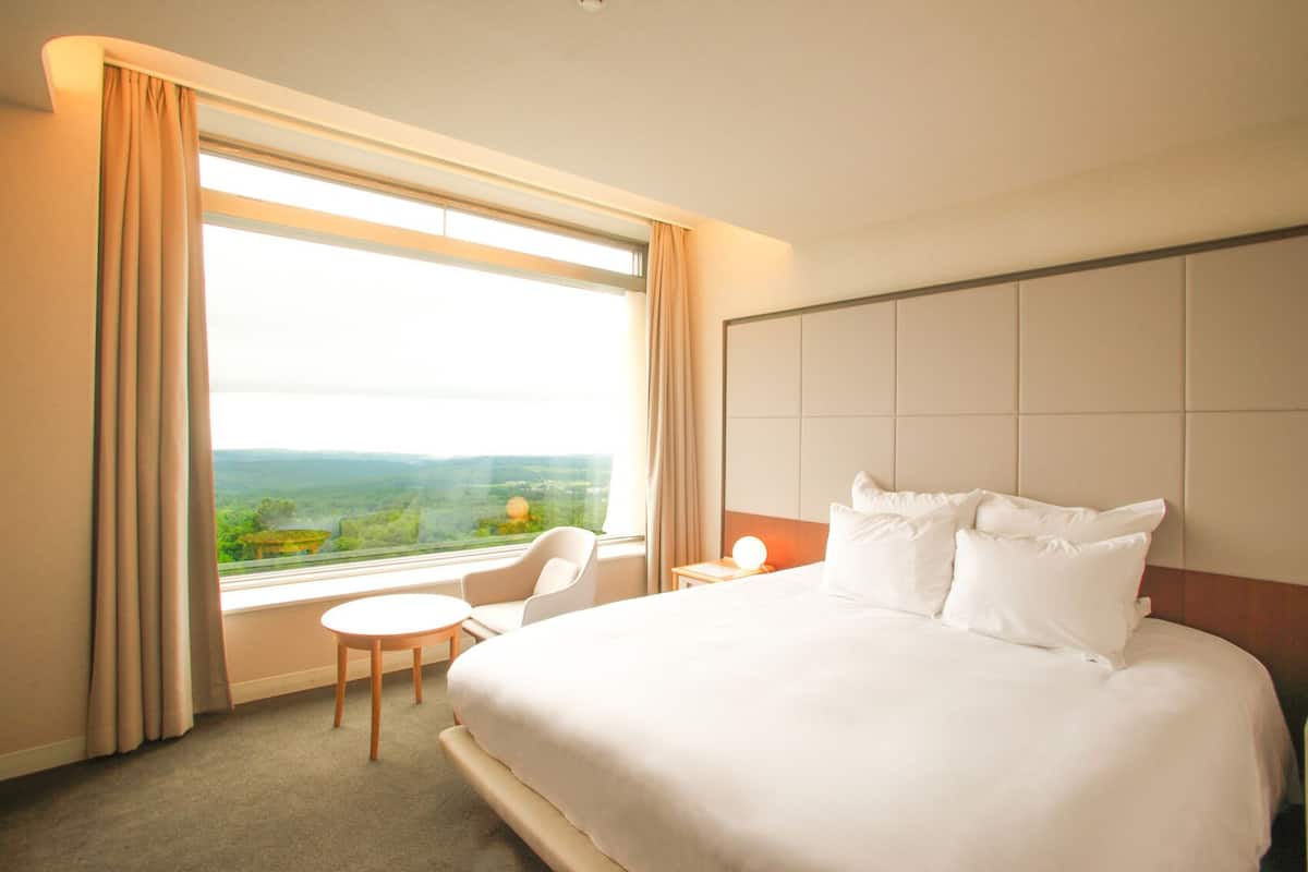 Une chambre d’hôtel avec un grand lit, une chaise, une table de chevet et une fenêtre avec des rideaux.