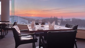 A dining table set for two with a view of a sunset over mountains.