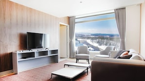 A modern living room with a flat-screen TV, a sofa, a chair, and a small table.
