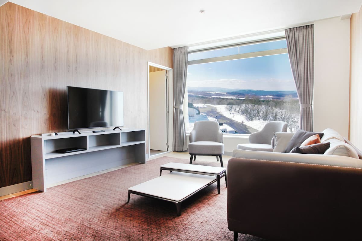 A modern living room with a flat-screen TV, a sofa, a chair, and a small table.