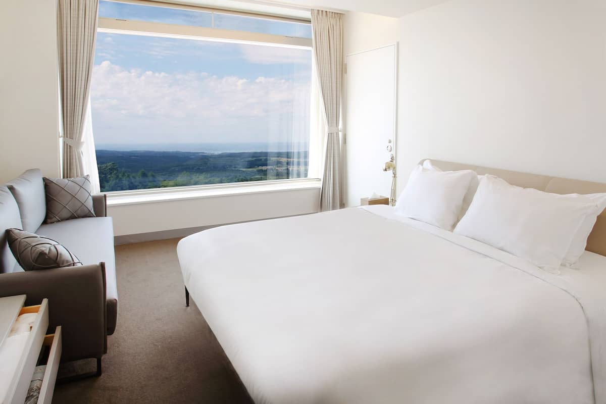Une chambre d’hôtel avec un grand lit, un canapé, une fenêtre donnant sur un beau paysage et une table de chevet.