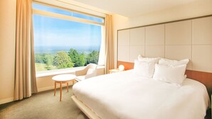 A hotel room with a large bed, a chair, a small table, and a view of the outdoors.