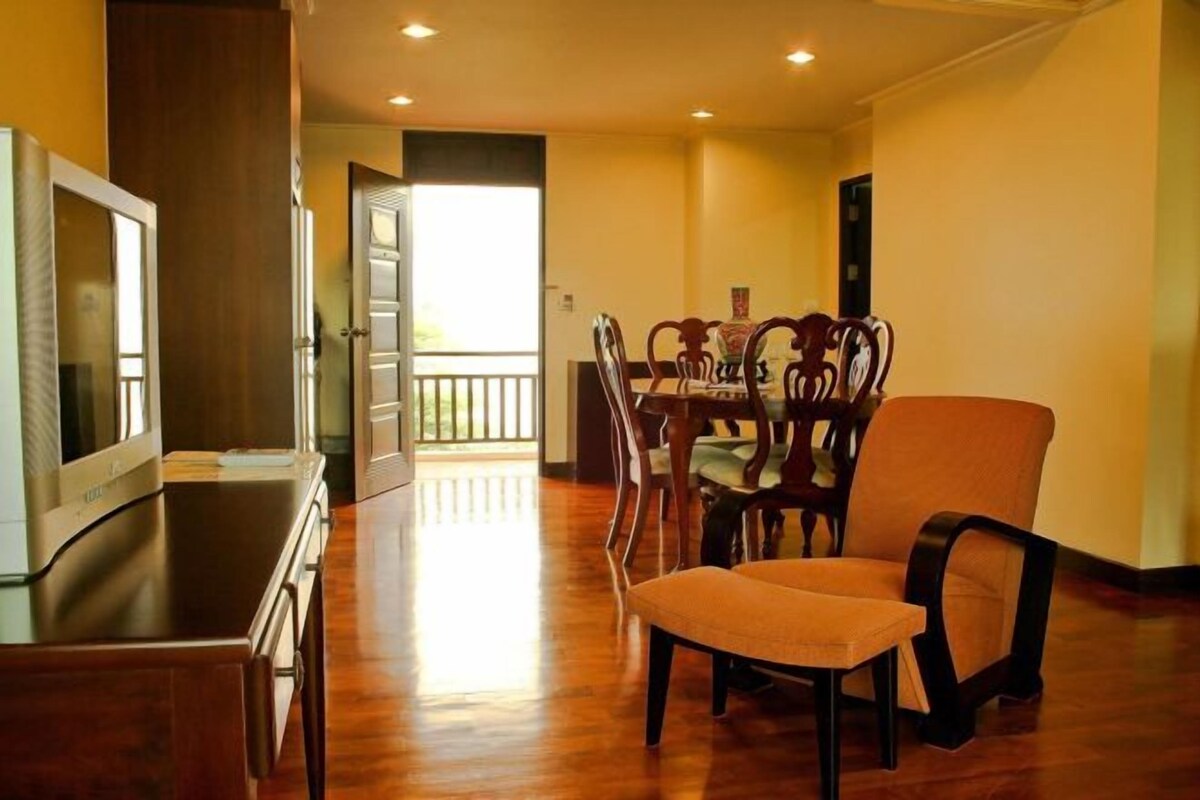 A dining area with wooden chairs and a table, a television on a stand, and a door leading to an outdoor balcony.