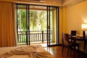 Una camera d'albergo con un letto, una scrivania con un portatile e vista su palme attraverso una porta scorrevole.