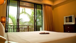 A hotel room with a bed, a TV on a wooden cabinet, and a large window with a view of palm trees. - Lecasa Bangsaen Hotel (Chonburi)